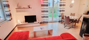 A modern living room with a red sofa, a flat-screen TV, a coffee table, and a dining area with a table and chairs.