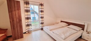 A bedroom with a bed, a nightstand, a wooden wardrobe, and a window with curtains.