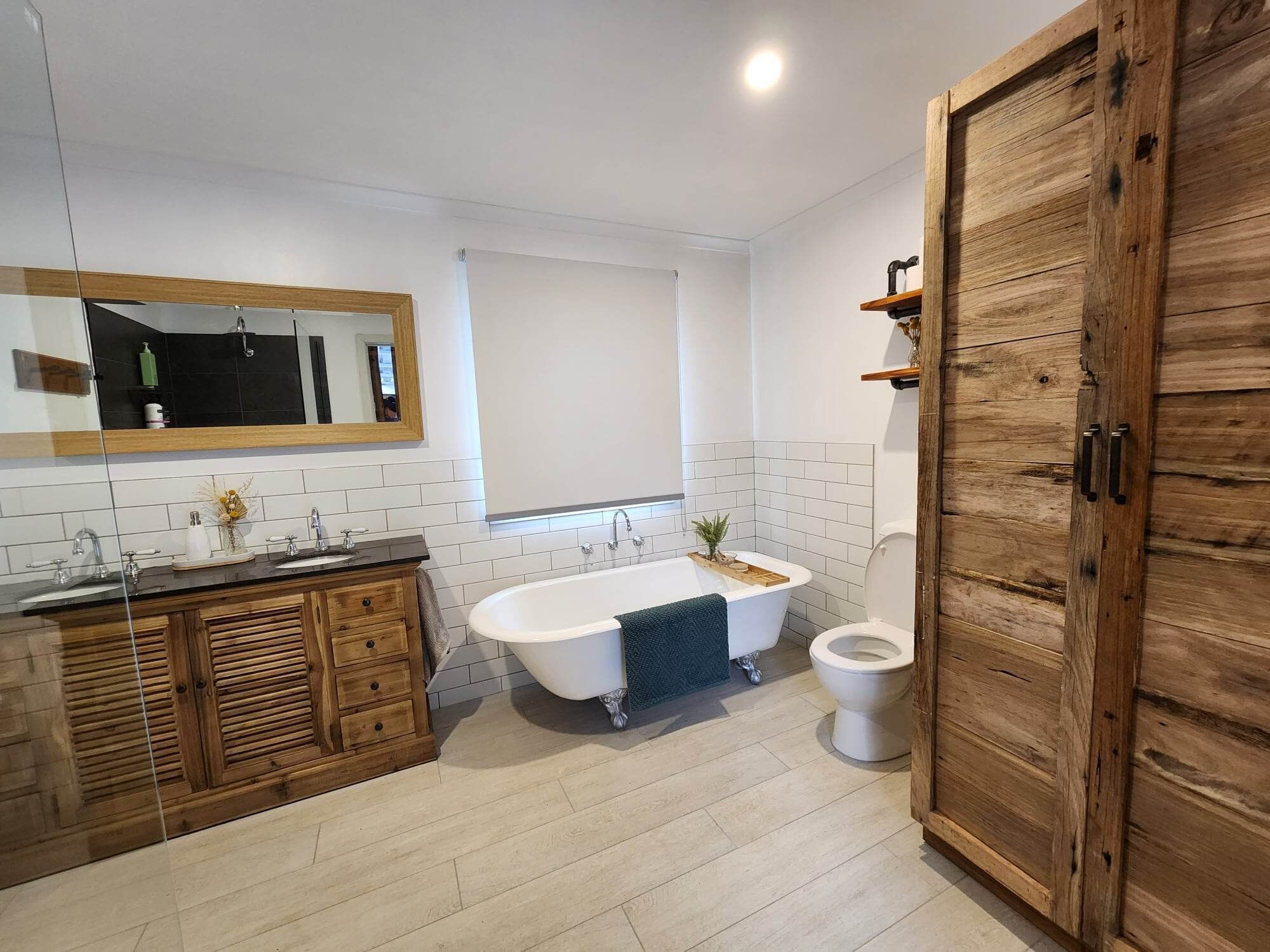 Une salle de bain moderne avec une baignoire sur pieds, un meuble-lavabo en bois, des toilettes et un grand miroir.