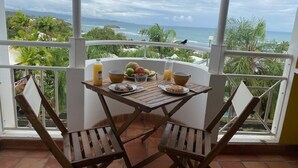 A dining area with a table set for two, overlooking a scenic ocean view. - Studio "le pipiri" swimming pool sea view secure residence (La Trinité)