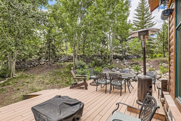 A wooden deck with outdoor furniture, a grill, and a stone wall in the background. - Private Waterdance Home with all the Amenities!! (Frisco)