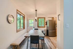 A kitchen with a wooden table, chairs, a clock, and a refrigerator.