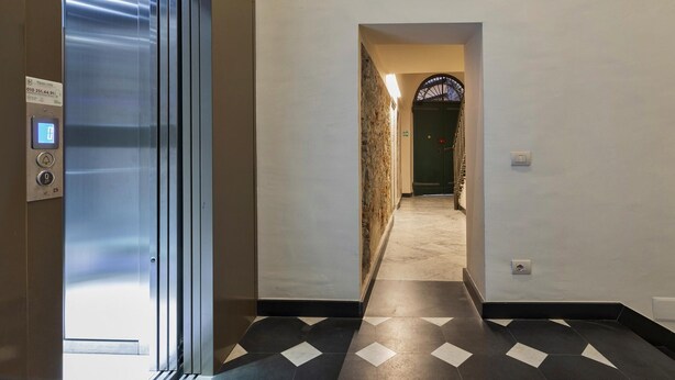 An interior hallway with a metallic elevator door, a stone wall, and a tiled floor. - Superba Studio by Wonderful Italy (Genoa)