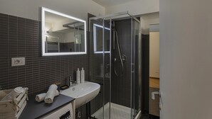 A modern bathroom with a glass-enclosed shower, a white sink, and a mirror above it. - Superba Studio by Wonderful Italy (Genoa)