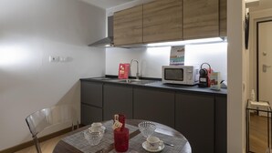 A compact kitchen with wooden cabinets, a microwave, a kettle, and a small dining table with a chair. - Superba Studio by Wonderful Italy (Genoa)