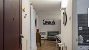 A hallway leading to a bedroom with a bed, a bedside table, and a wall-mounted clock. - Superba Studio by Wonderful Italy (Genoa)