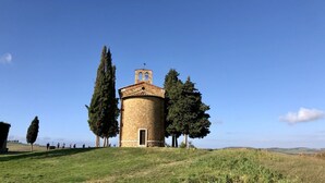 A stone tower with a bell on top, surrounded by trees, set in a grassy field.
