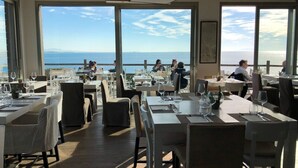 A restaurant with tables set for dining, large windows offering a view of the sea, and a calm atmosphere.