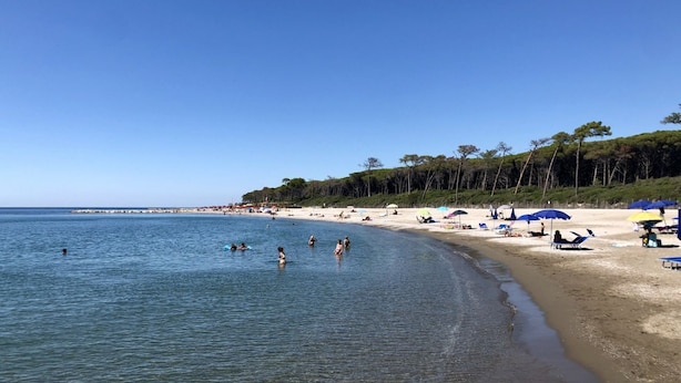 A beach with clear blue water, people swimming and sunbathing, and beach umbrellas.