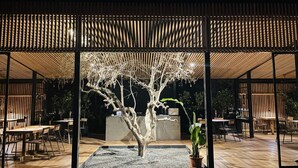 A modern outdoor seating area with a wooden structure, a central tree, and a gravel path.