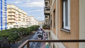 A street view from a balcony overlooking a multi-story building with a bar sign, trees, and parked vehicles. - Beauty Design in the Center by Wonderful Italy (Genoa)