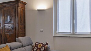 A living room with a grey sectional sofa, a wooden cabinet, and a window with blinds. - Beauty Design in the Center by Wonderful Italy (Genoa)