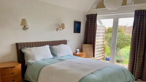 A bedroom with a bed, bedside tables, a lamp, a chair, and a view of the outdoors.