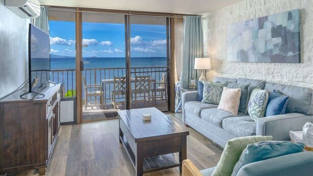 Un salon avec un canapé, une table basse et un téléviseur. Il y a un balcon avec vue sur la mer.