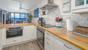 Une cuisine moderne avec des meubles blancs, un plan de travail en bois, un four encastré et une vue sur l’extérieur.