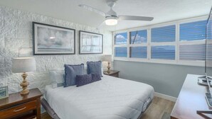 Une chambre à coucher avec un lit, des tables de chevet, un ventilateur de plafond et une fenêtre avec des stores.
