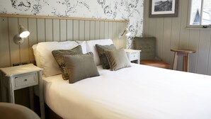 A neatly made bed with white linens and two pillows, flanked by two bedside tables with lamps. A framed picture hangs on the wall above the bed. - Castle Inn By Greene King Inns (Bakewell)