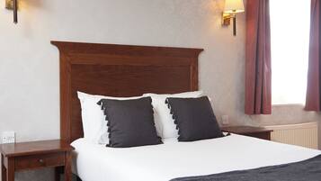 A neatly made bed with a wooden headboard, two bedside tables with lamps, and a window with curtains.