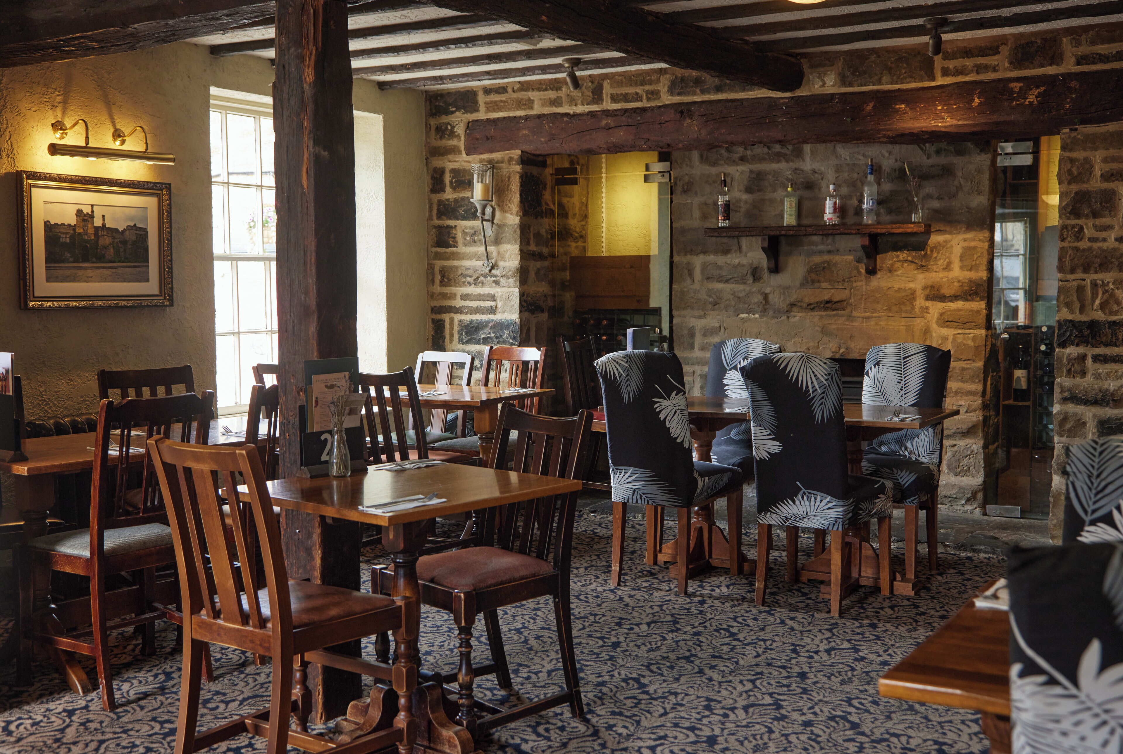 A rustic dining area with wooden tables and chairs, stone walls, and a patterned floor.