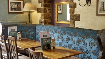 A restaurant interior with wooden tables and benches, menu stands, and wall-mounted lamps.