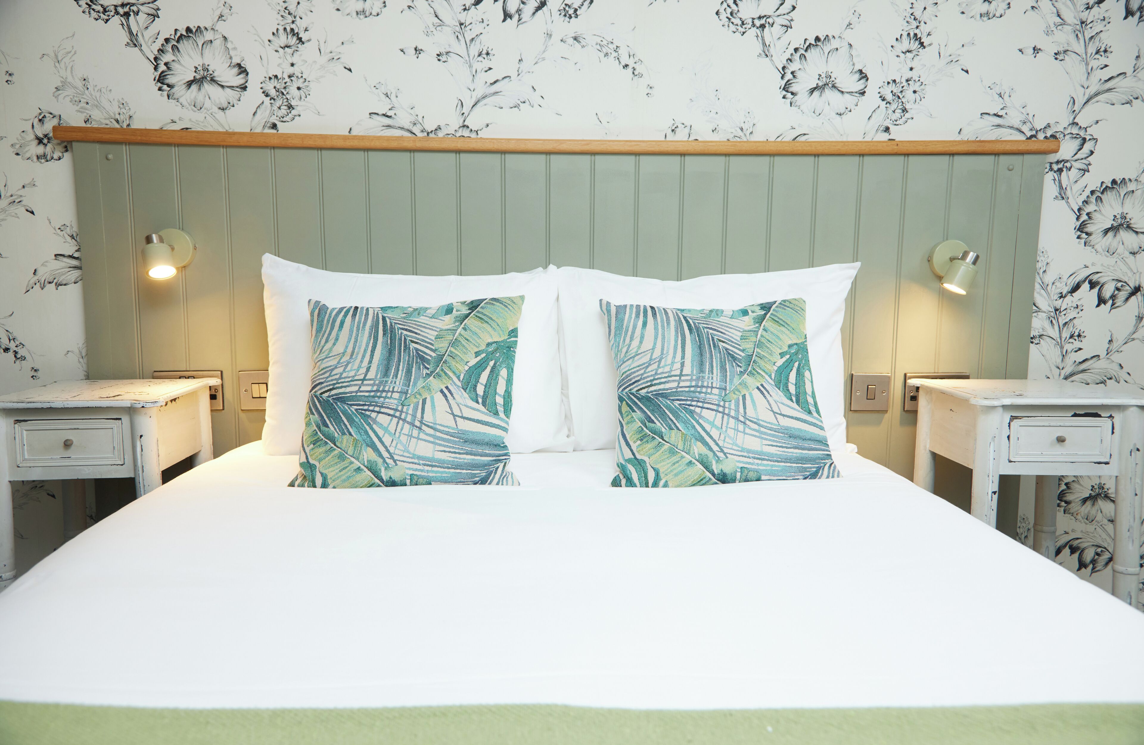 A neatly made bed with two pillows, a wooden headboard, and two bedside tables with lamps.