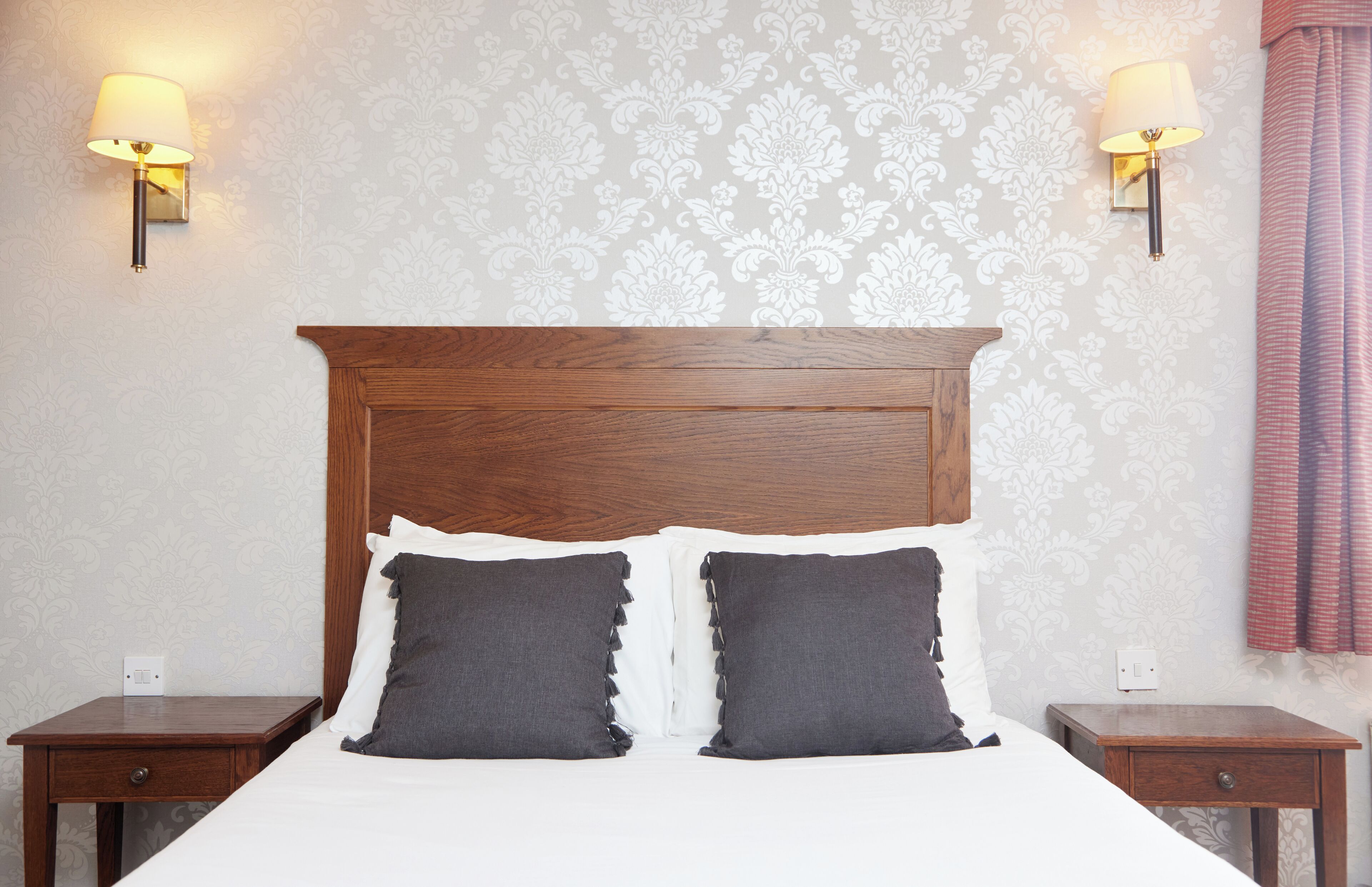 A neatly made bed with a wooden headboard, two bedside tables, and wall-mounted lamps.