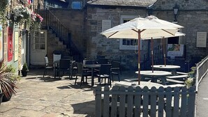 A stone building with a flag, outdoor seating, and a staircase. - Castle Inn By Greene King Inns (Bakewell)