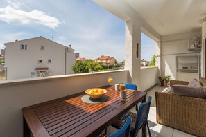 Un balcon avec une table en bois, un canapé en osier et un saladier rempli de fruits.
