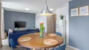 Una zona de menjador moderna amb una taula rodona de fusta, cadires blaves i una làmpada penjant.