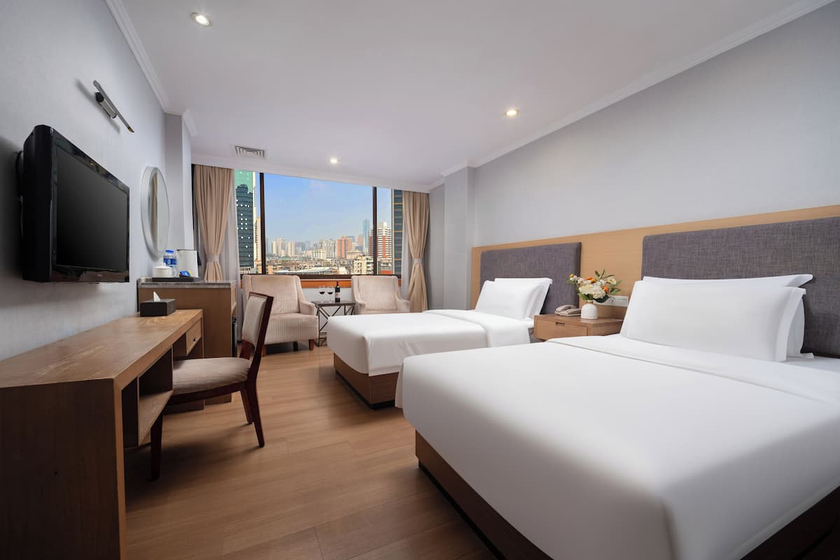 A hotel room with two beds, a desk, a TV, and a view of the city skyline.