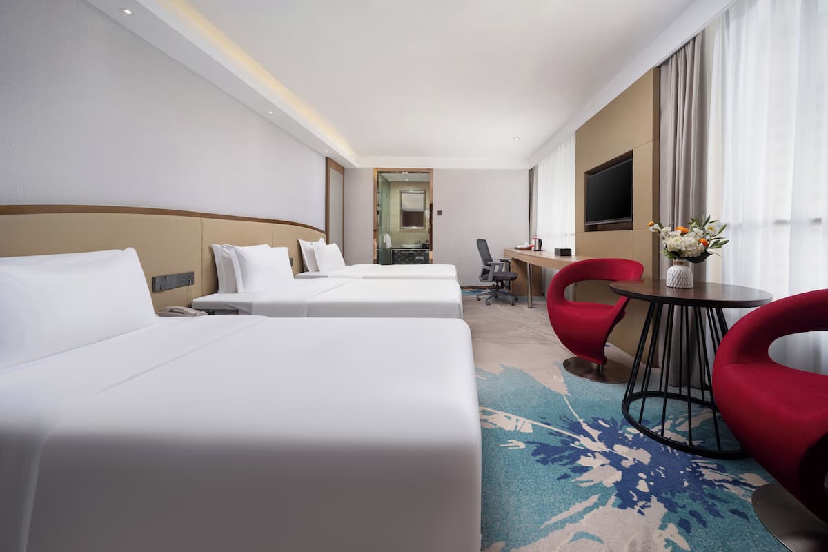 A hotel room with two beds, a desk, a chair, and a TV.