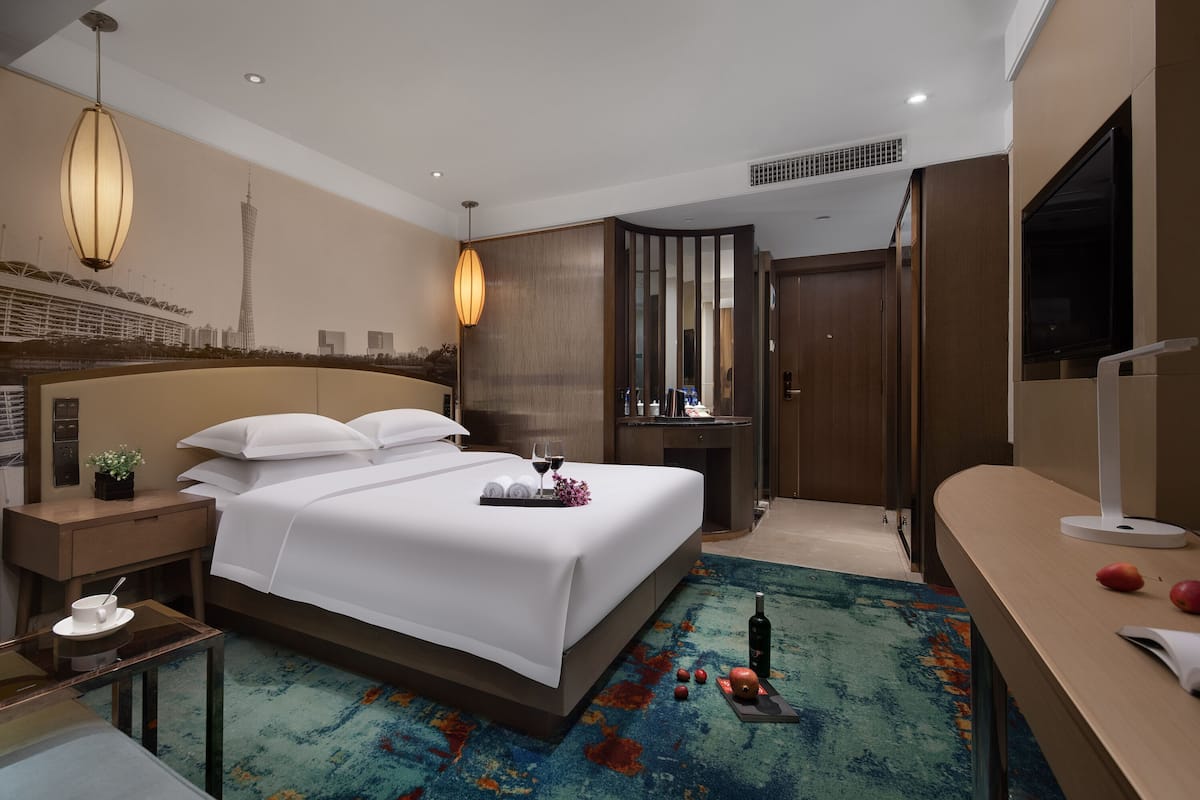 A hotel room with a bed, bedside table, nightstand, and a large window.