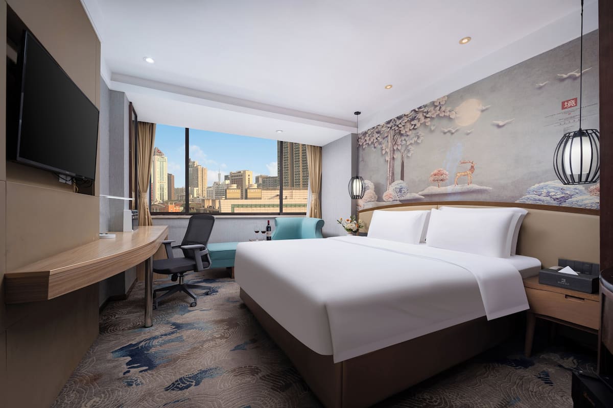 A hotel room with a large bed, a desk, a TV, and a city view.