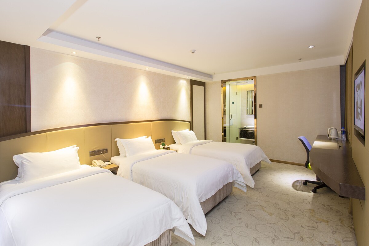 A hotel room with three beds, a desk, and a mirror.