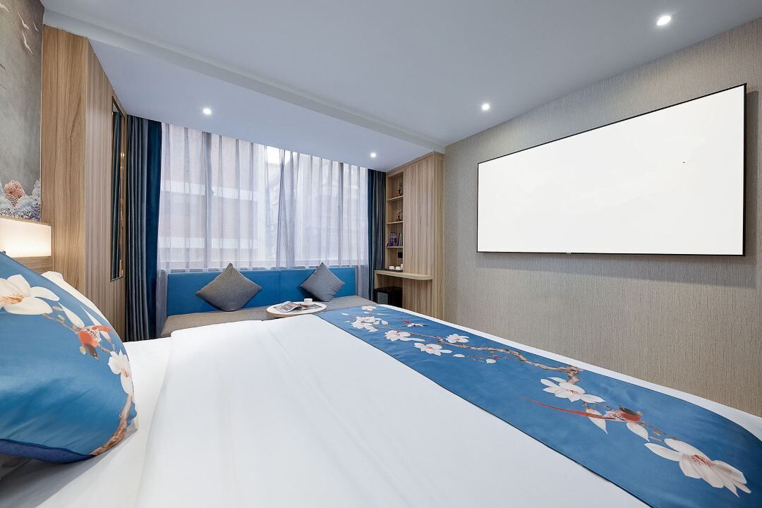 A hotel room with a bed, a TV, a bookshelf, and a window with curtains.