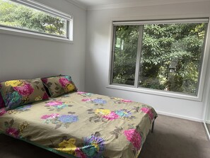 Une chambre à coucher avec une couvre-lit à motifs floraux, deux oreillers, une fenêtre donnant sur des arbres et un sol recouvert de moquette.
