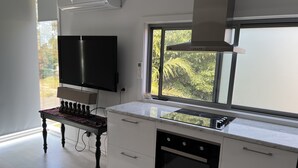 Moderni keittiö, jossa on sisäänrakennettu uuni, suuri ikkuna, josta avautuu näkymä vehreään maisemaan, sekä seinälle asennettu litteänäyttöinen televisio.
