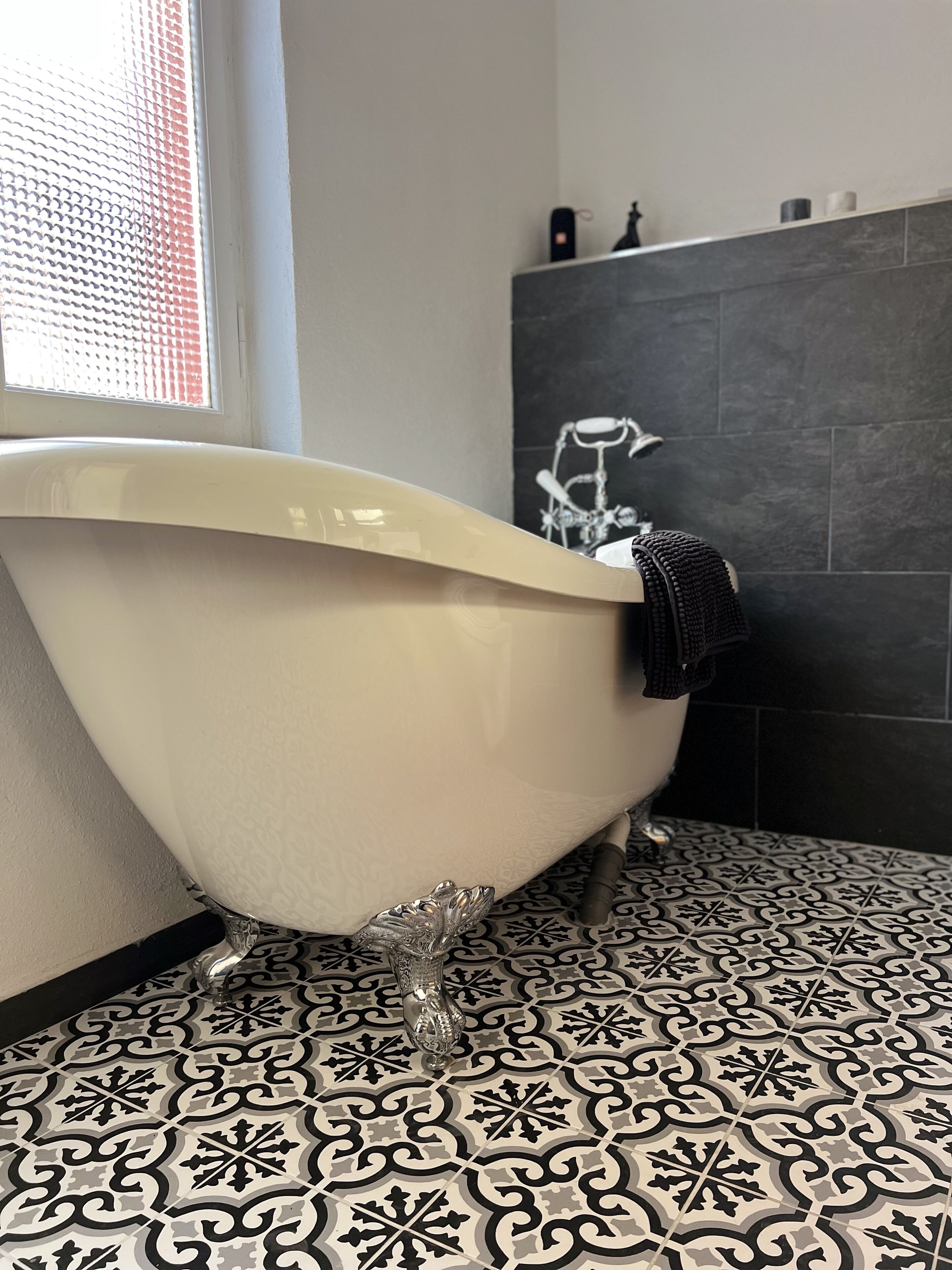 A bathroom with a freestanding bathtub, a patterned floor, and a dark tiled wall.