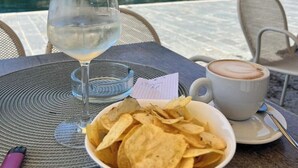 A table with a glass of water, a bowl of chips, and a cup of coffee, overlooking a lake with buildings and greenery in the background. - Old town Villa Rustico vacation home 600 meters to the SEE CASA LINDNER 14Guest (Maderno)