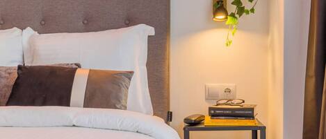 A neatly made bed with white and brown bedding, a bedside table with a lamp, a vase, and a stack of books.