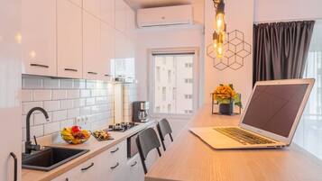 A modern kitchen with white cabinets, a wooden countertop, a laptop, and a coffee maker.