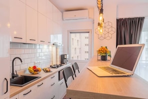 A modern kitchen with white cabinets, a wooden countertop, a laptop, and a coffee maker.