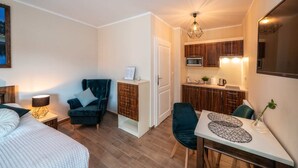 A compact room with a bed, a chair, a small table, a kitchenette, and a ceiling light. - Apartments 17 Szewska (Kraków)