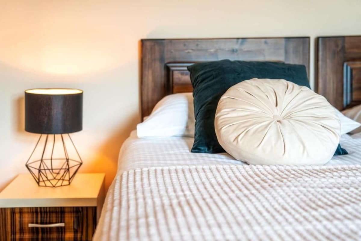 A neatly made bed with a patterned bedspread, a bedside lamp, and a wooden headboard.