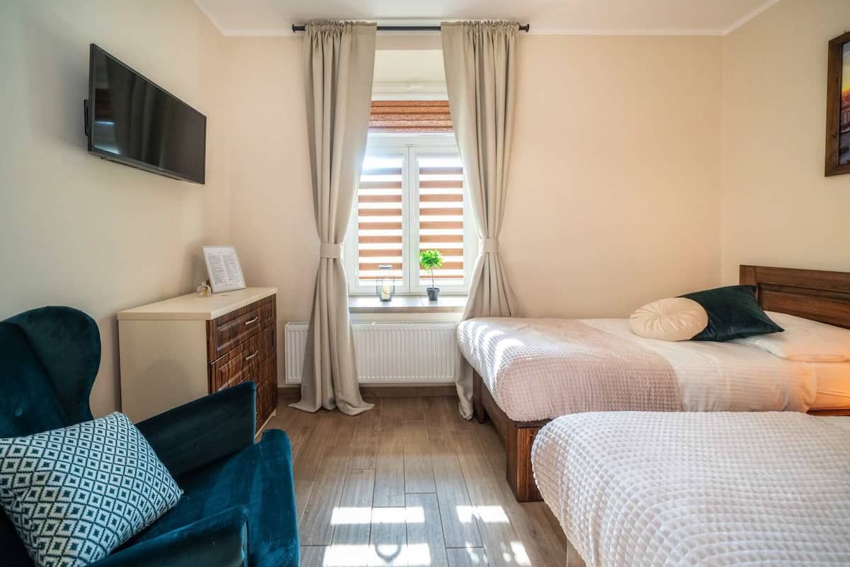A bedroom with two beds, a TV mounted on the wall, a desk with a chair, and a window with curtains.