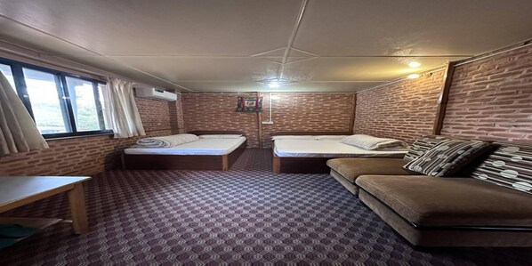 A room with two beds, a sofa, a small table, and brick-patterned walls. - MeroStay 031 Hotel Green Land (Bhaktapur)