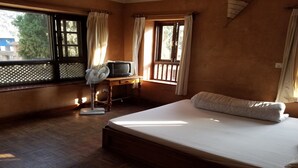 Une chambre à coucher avec un lit, un bureau avec une télévision et une fenêtre avec des rideaux.