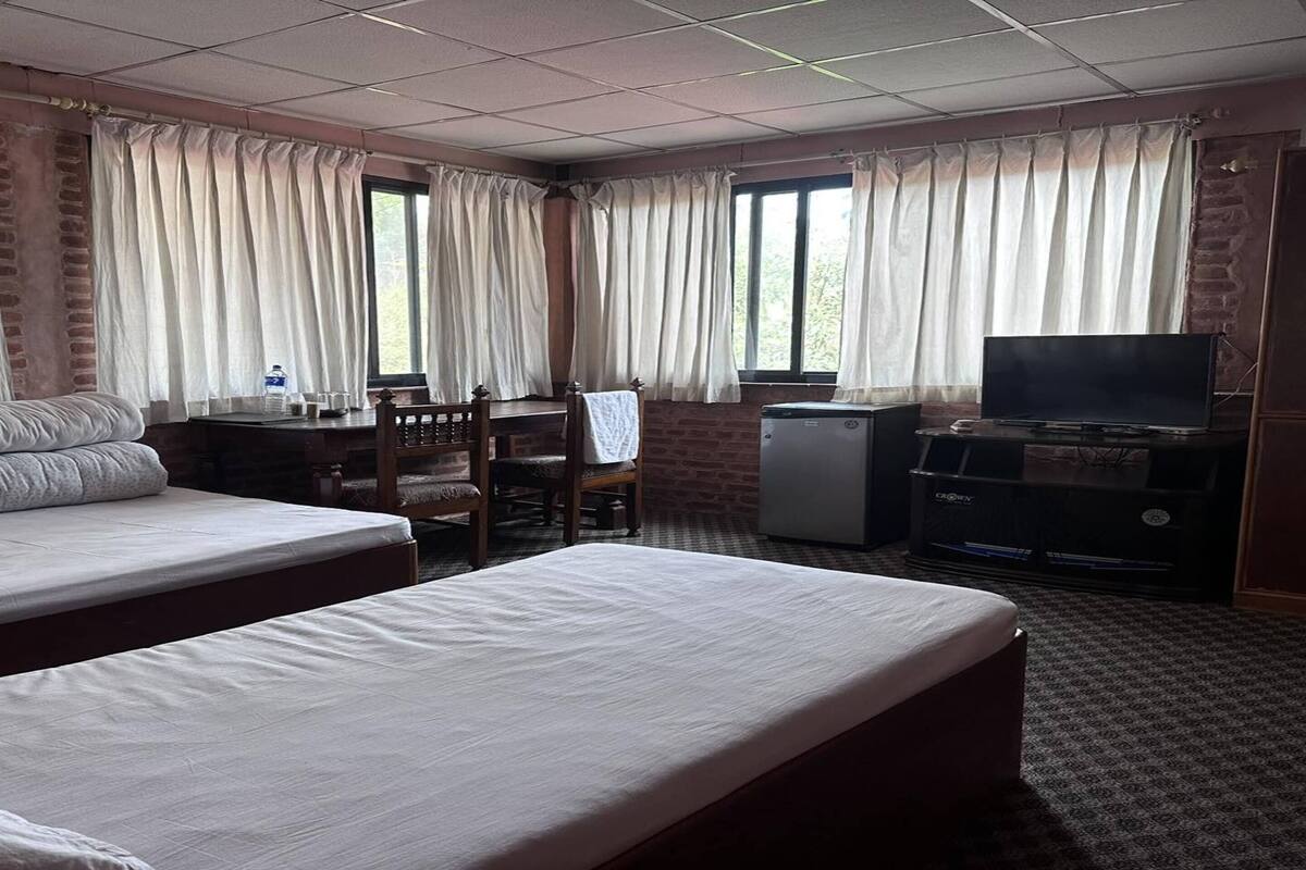 Een hotelkamer met twee bedden, een bureau, een televisie en een raam met gordijnen.
