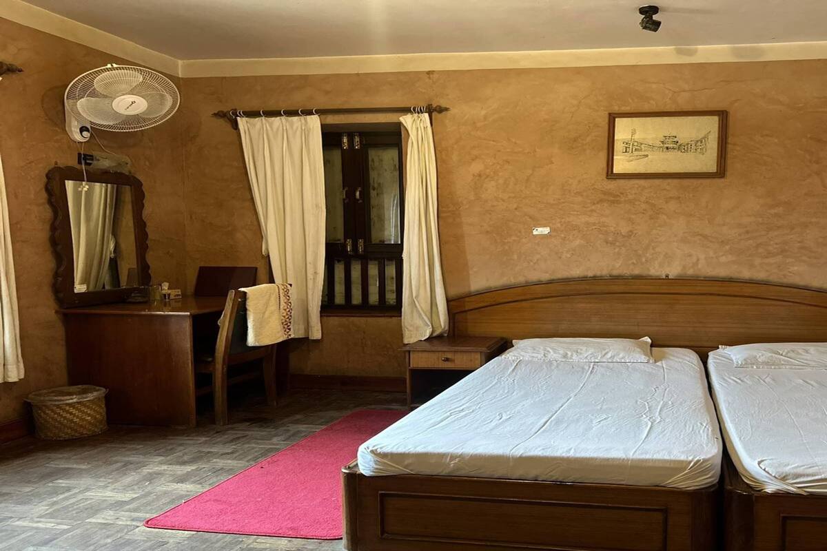 Een slaapkamer met twee bedden, een houten hoofdbord, een nachtkastje, een spiegel, een ventilator en een raam met gordijnen.