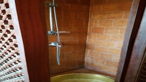 Un petit espace douche fermé, avec un mur carrelé et une pomme de douche en métal.